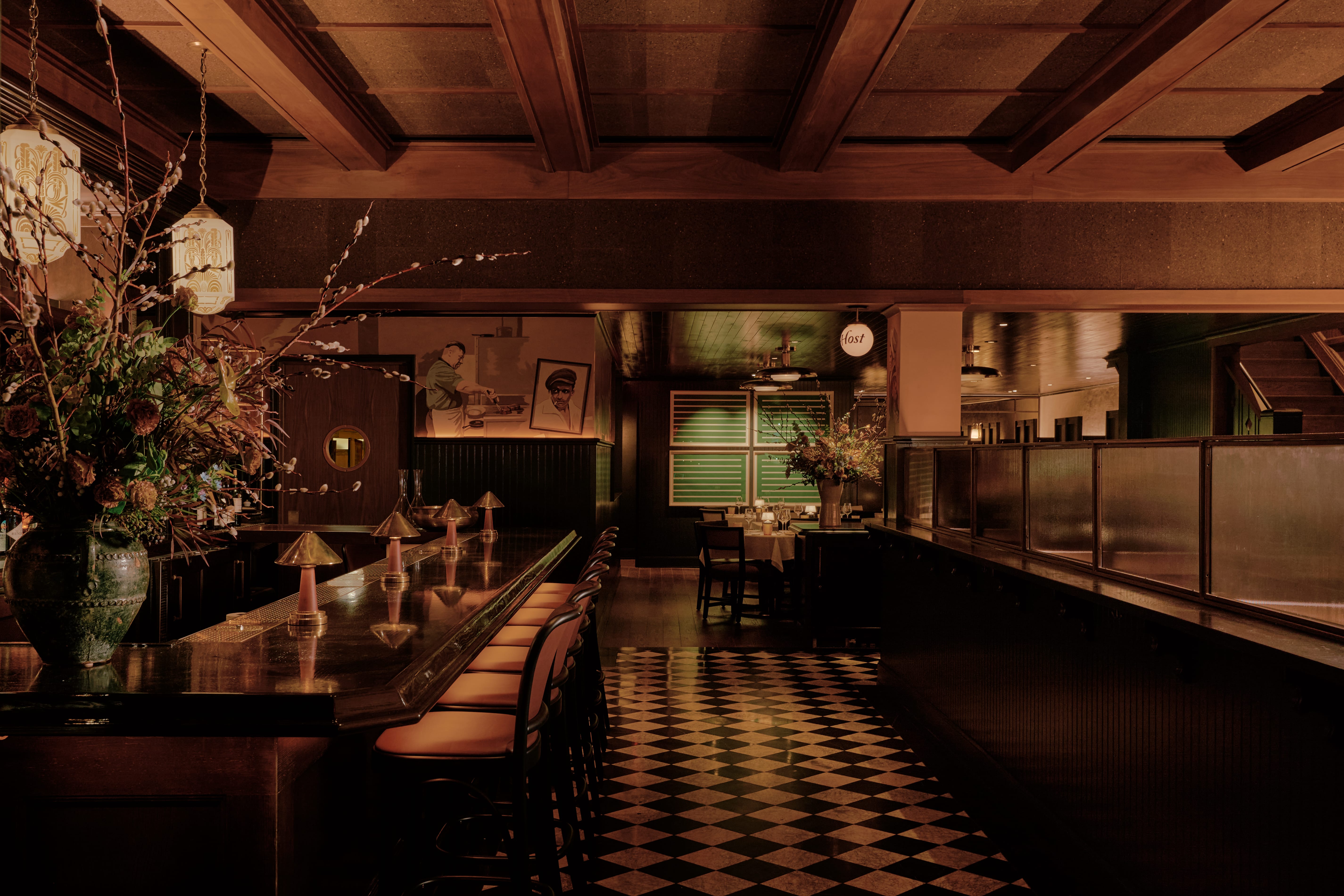 Wide-angle interior of Izzy's restaurant — long dark wood bar, checkered floors, pendant lighting, and flowers