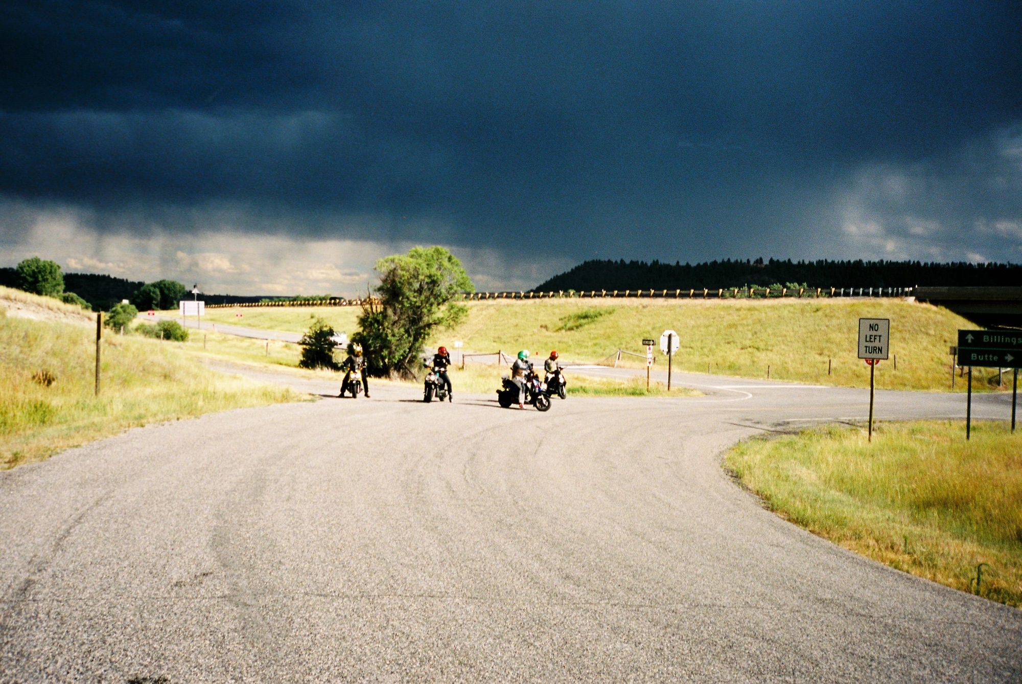 Film photo of riders gathering at a rural intersection under dramatic dark storm clouds