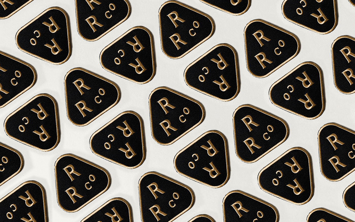 Repeat pattern of black and gold Rainier Roofing enamel patches on white background