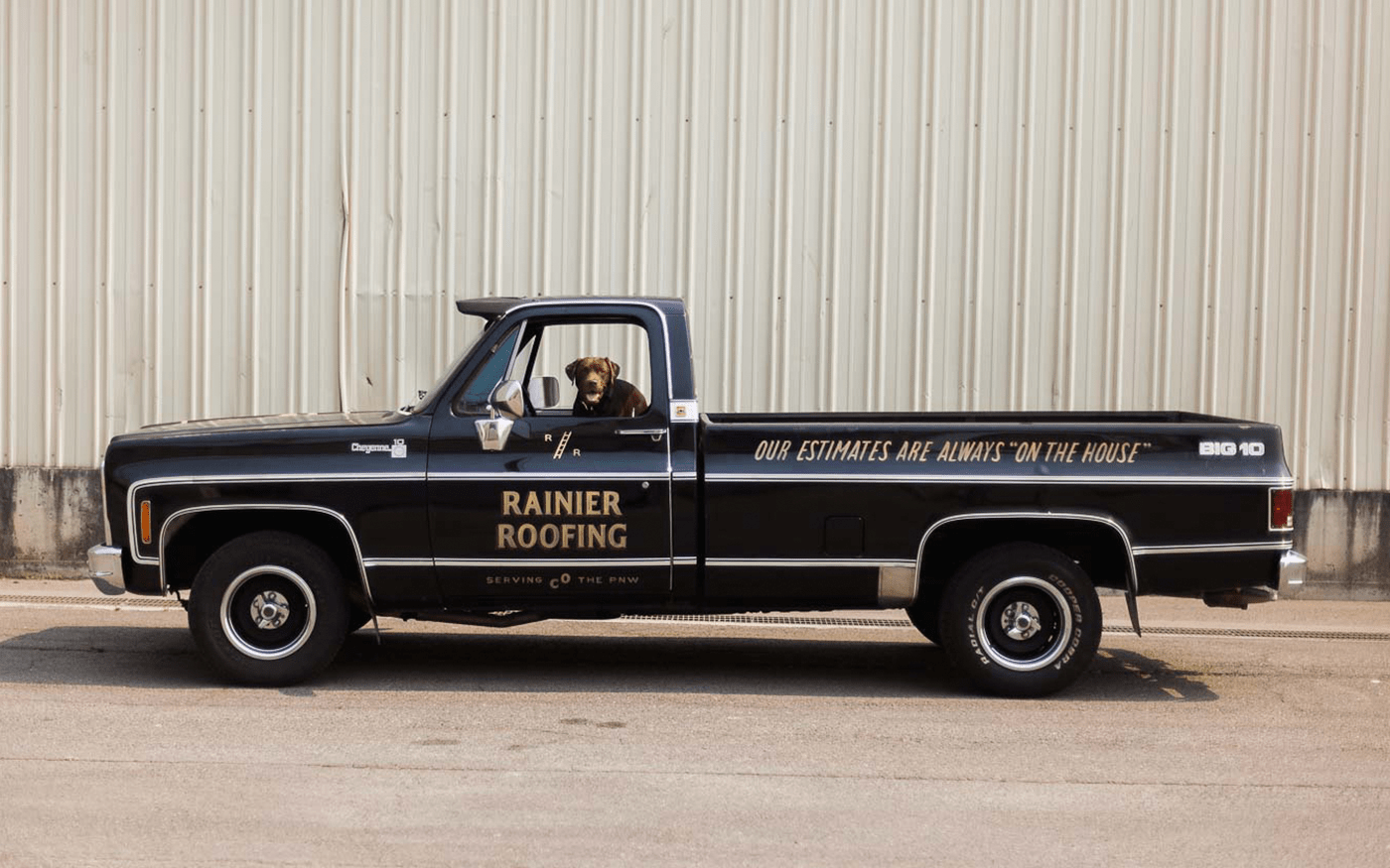 Side view of a vintage black Rainier Roofing pickup truck with 'Our estimates are always on the house' tagline