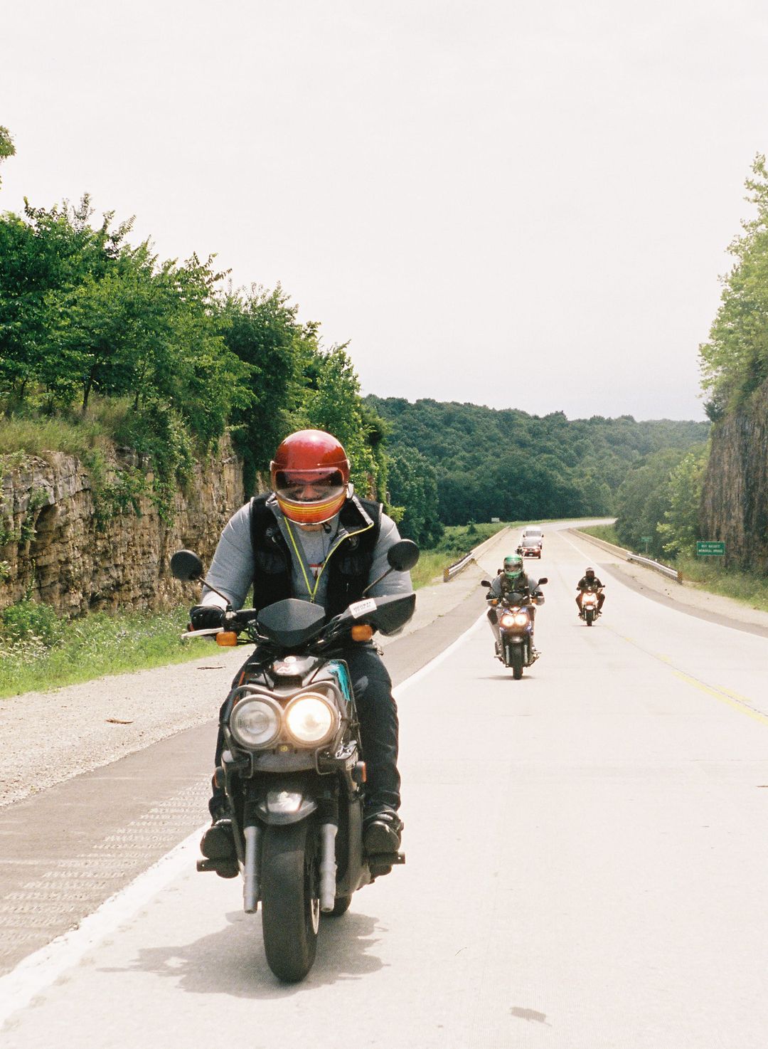 Film photo of three motorcyclists riding in formation through a lush tree-lined highway