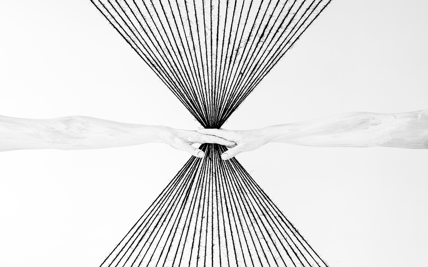 Black and white fine art photo of two forearms reaching from opposite sides with hands clasped at center and radiating string lines forming an hourglass shape