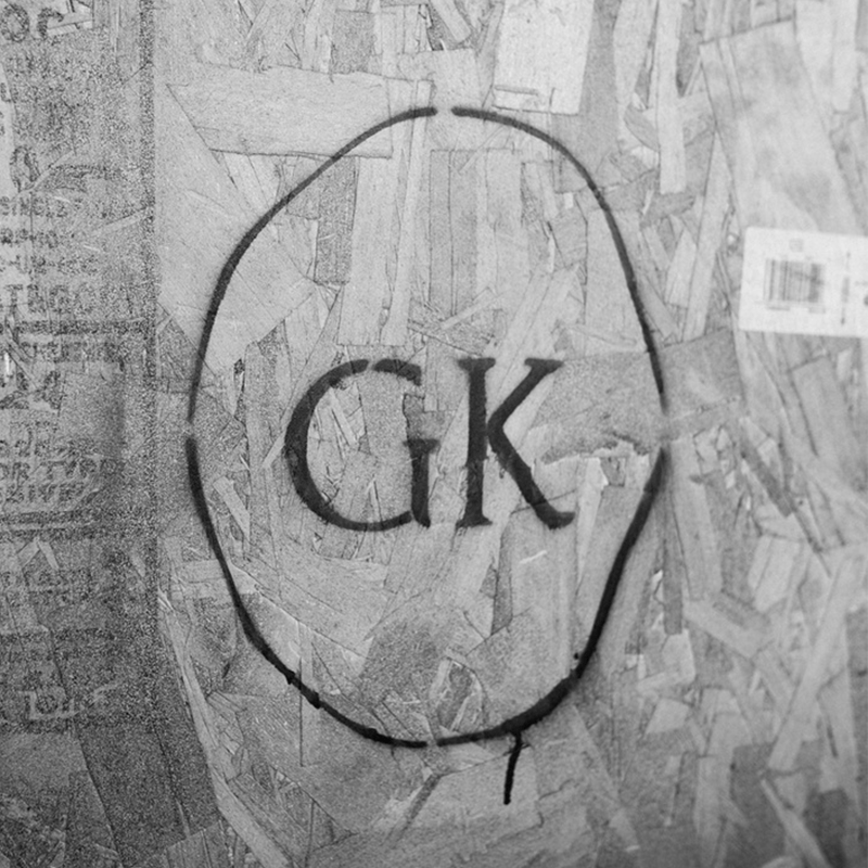 GK oval logo spray-painted in black on a textured cardboard surface