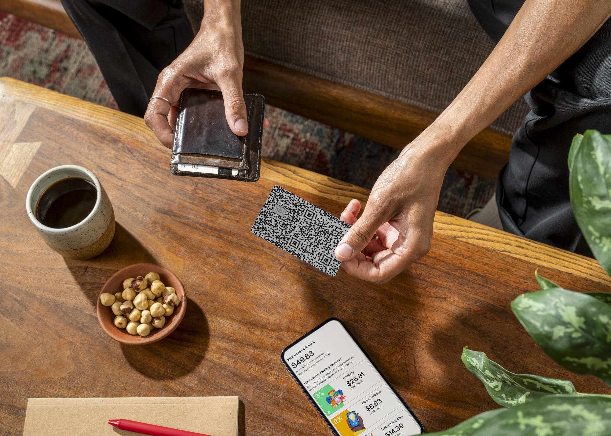 Overhead view of person removing a black QR-code Venmo card from a slim card wallet at a wooden desk with Venmo app open on phone