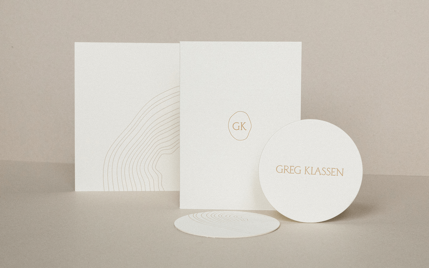 Greg Klassen stationery set — square folder with GK oval emblem and round coaster arranged on a neutral background