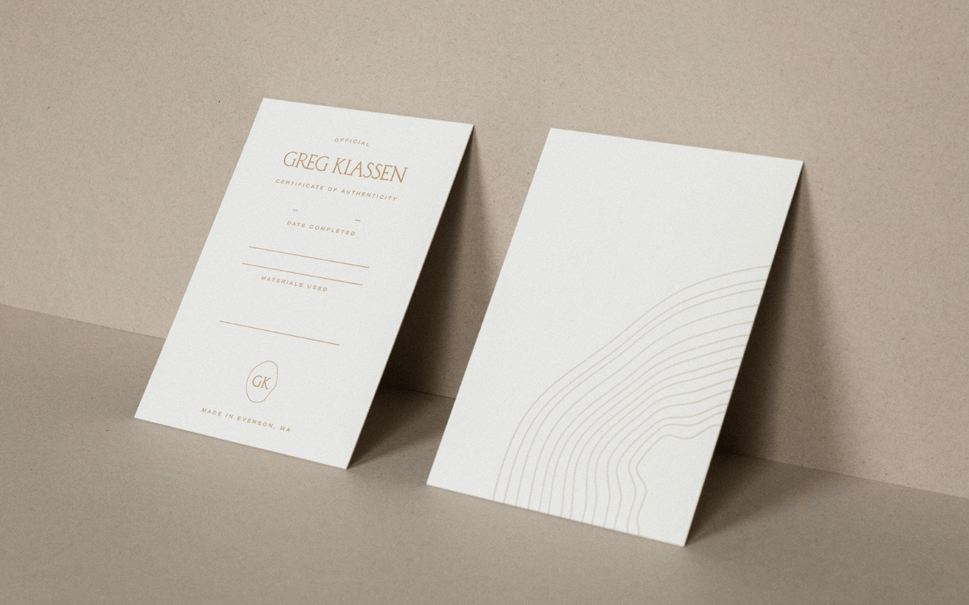 Two cream Greg Klassen business cards standing upright showing front with name and contact info and back with arc line graphic