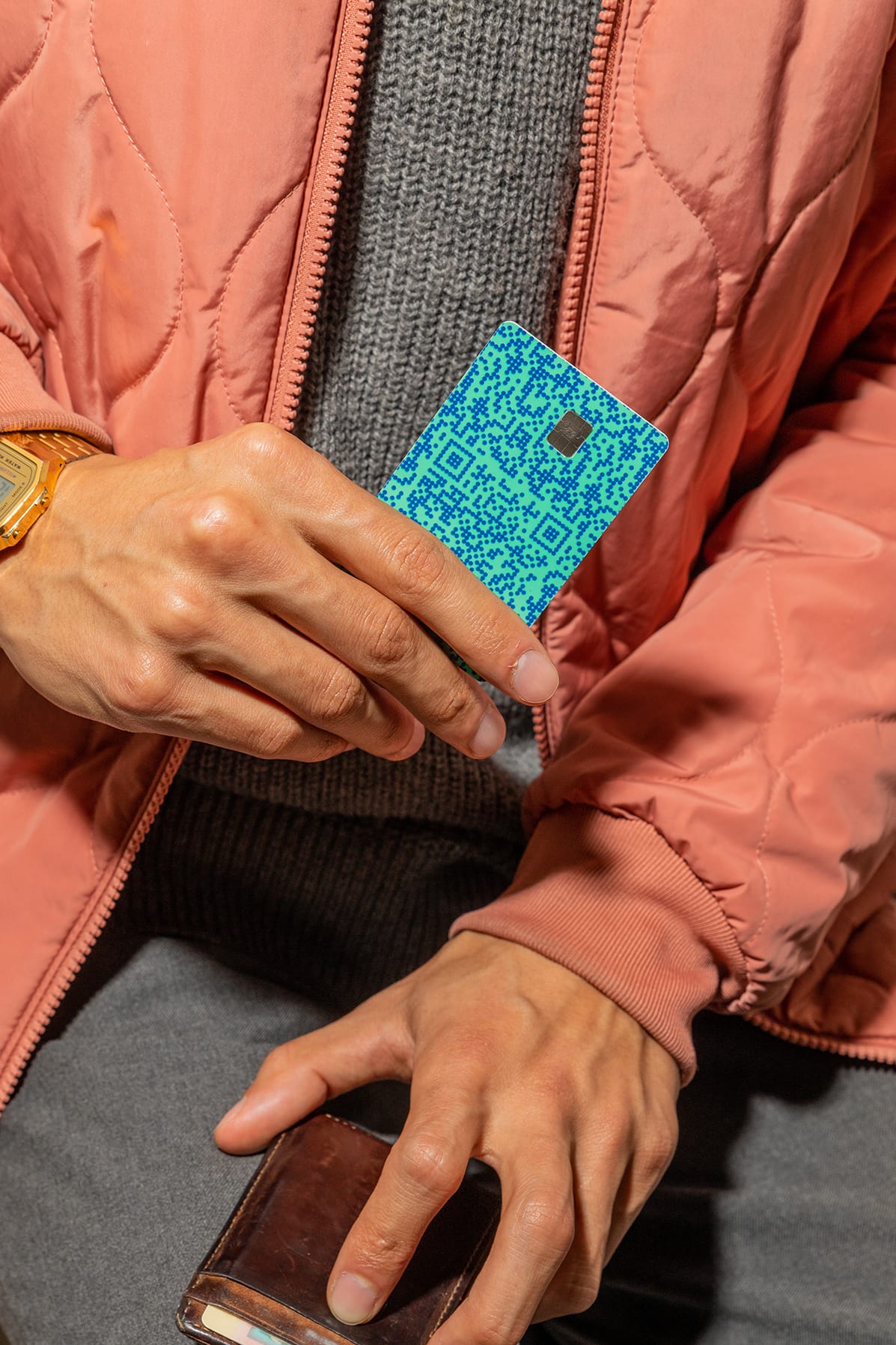 Person in a salmon puffer jacket holding a blue-green Venmo card with a leather wallet in their other hand