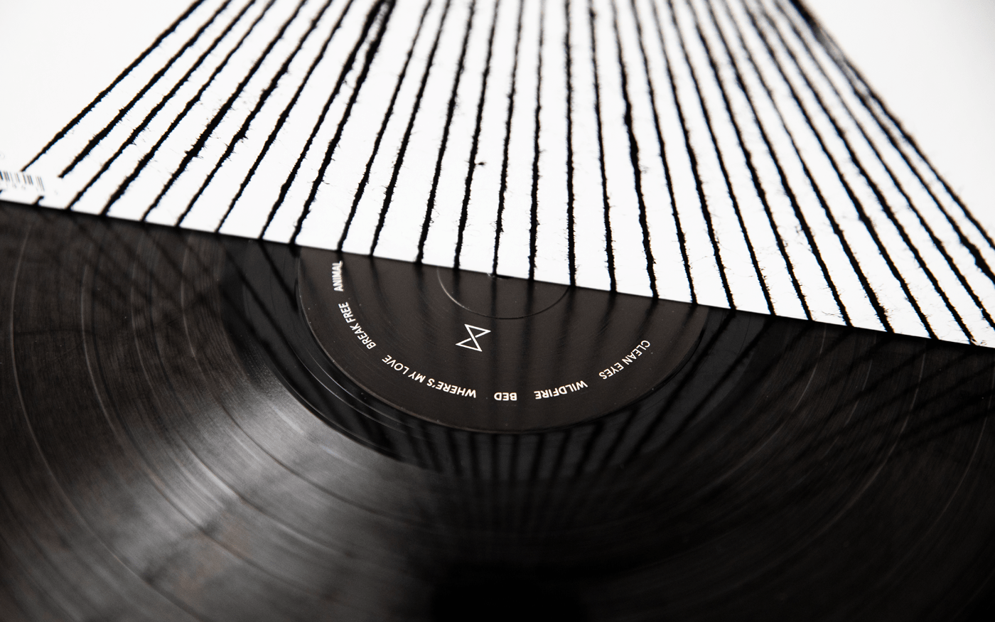 Close-up of a vinyl record partially pulled from its sleeve — sleeve features thin vertical black lines, record label shows SYML branding