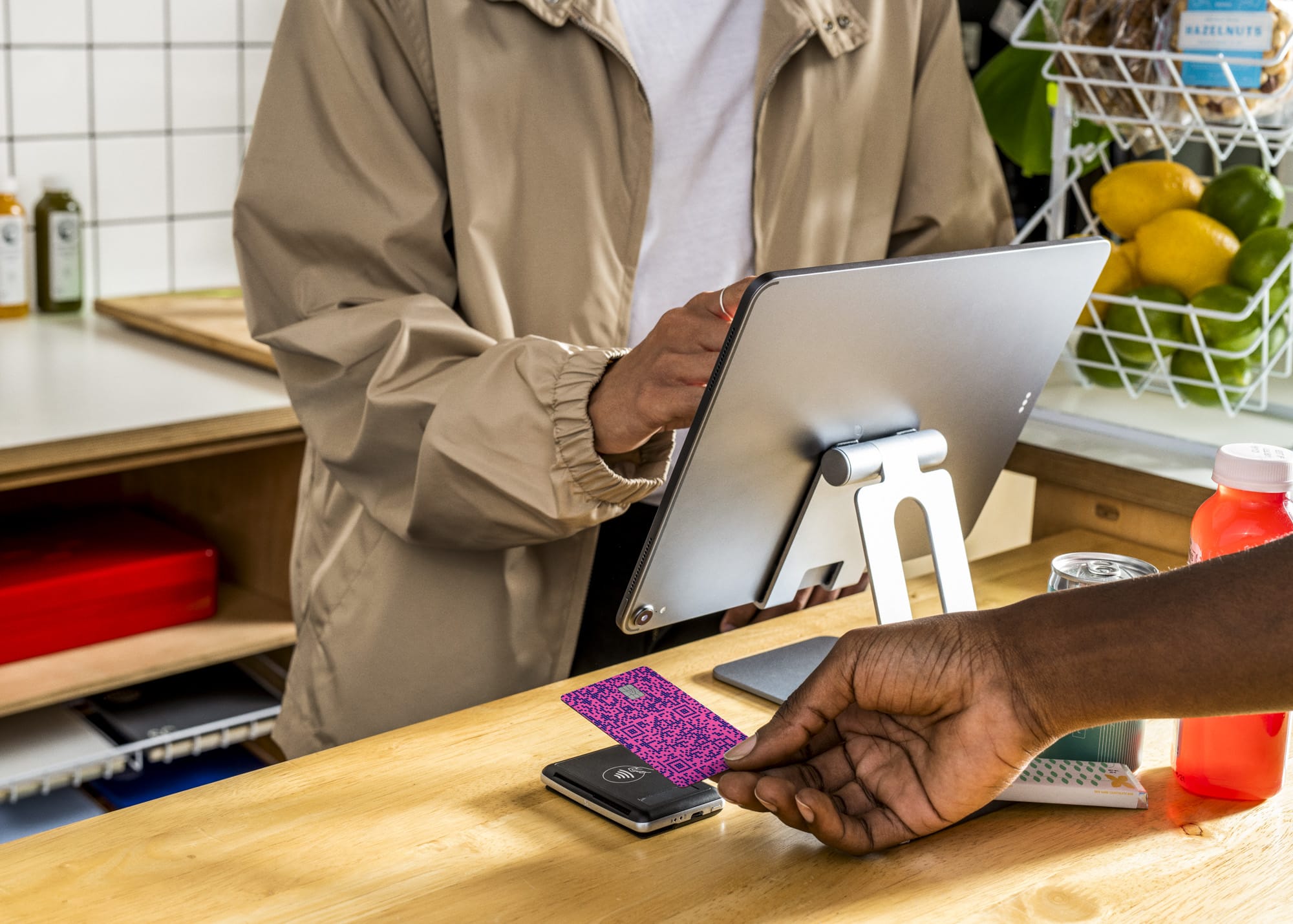 Person tapping a pink QR-code Venmo card on a card reader at a market counter while cashier holds a tablet