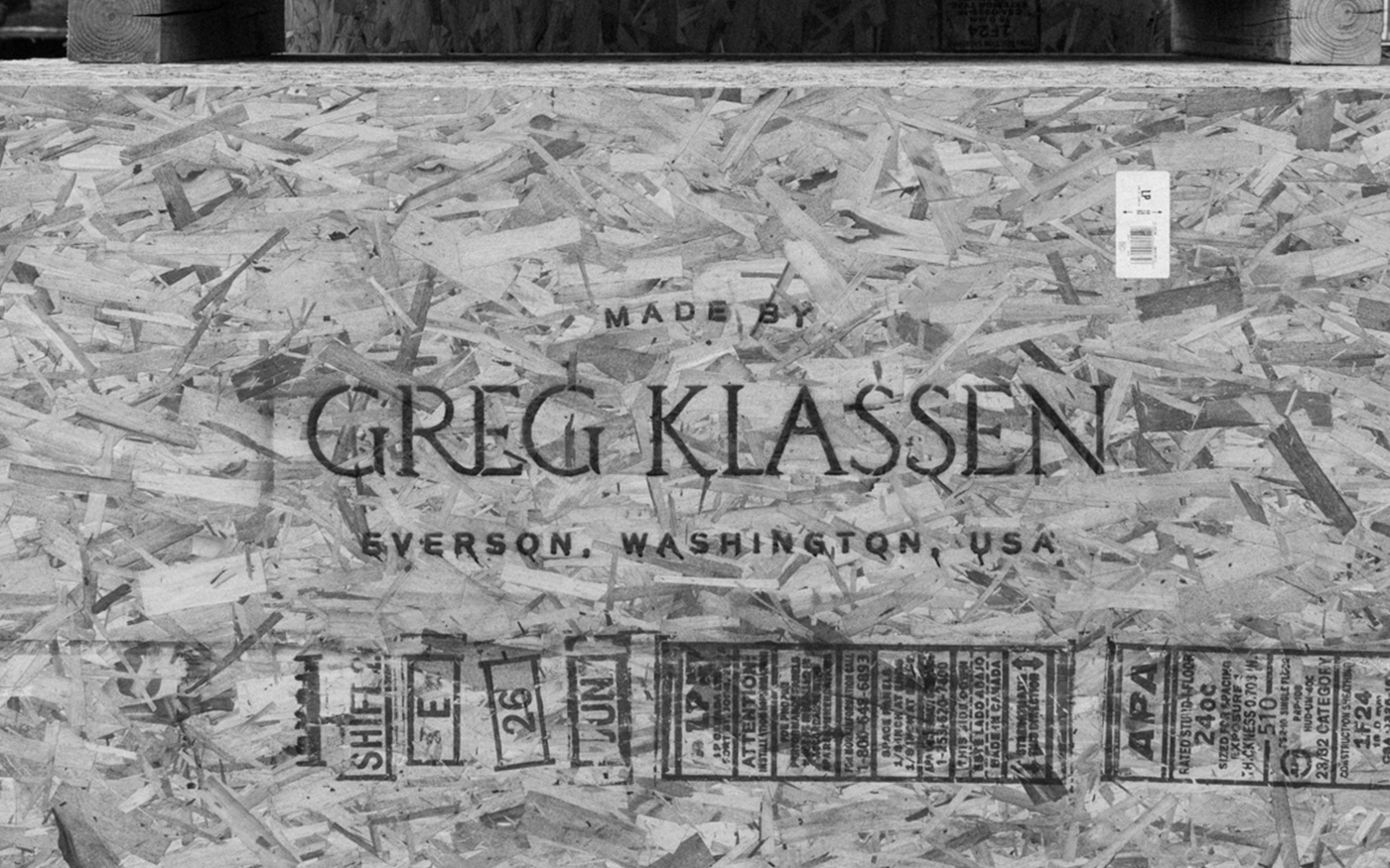 Stenciled text reading Made by Greg Klassen, Everson, Washington, USA on an oriented strand board surface
