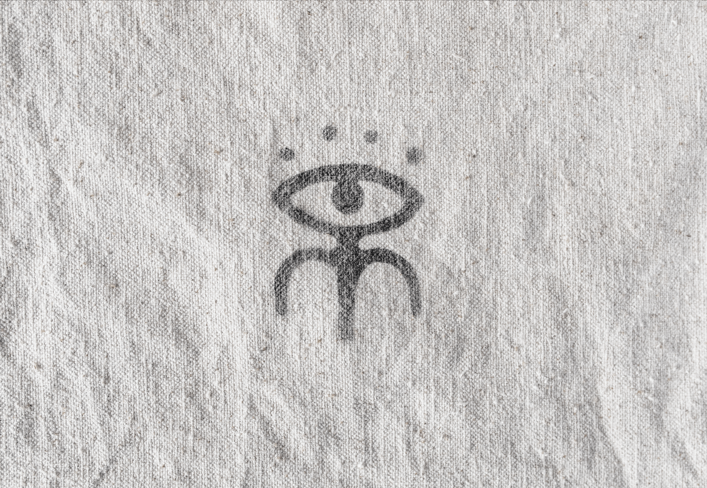 De Melo eye and figure icon stamp pressed in gray on wrinkled linen fabric