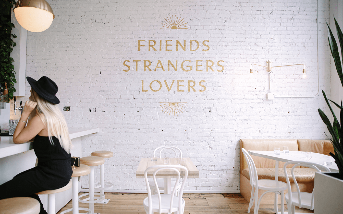 Bright white restaurant interior with Friends Strangers Lovers painted in gold script on a white brick wall