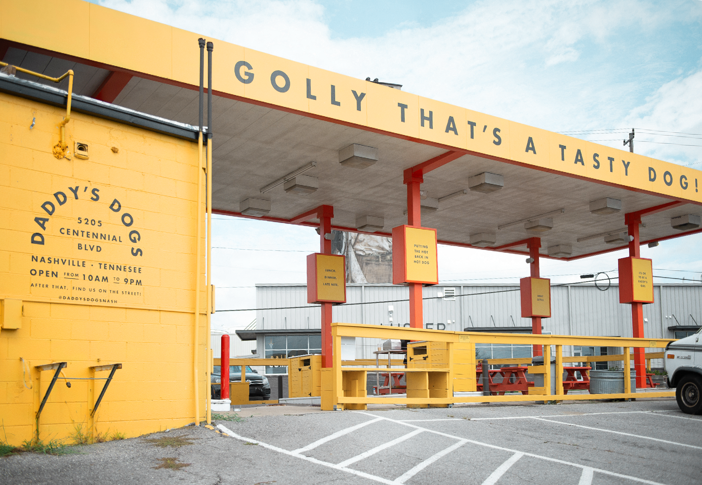 Wide shot of yellow Daddy's Dogs building with a gas station canopy and Golly That's a Tasty Dog banner visible