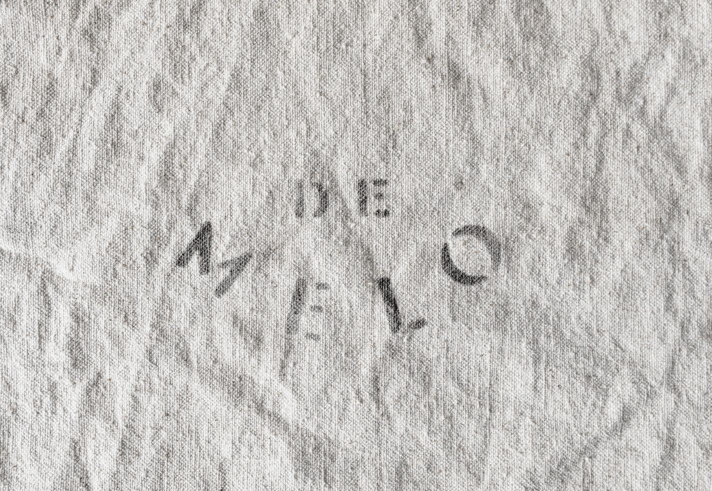 De Melo brand name stamped in gray ink on wrinkled linen fabric