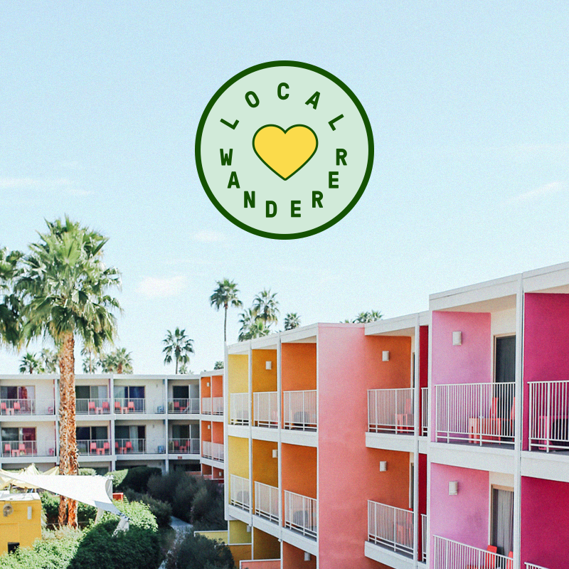 Colorful pink and orange motel exterior with Local Wanderer heart logo overlaid in green above it