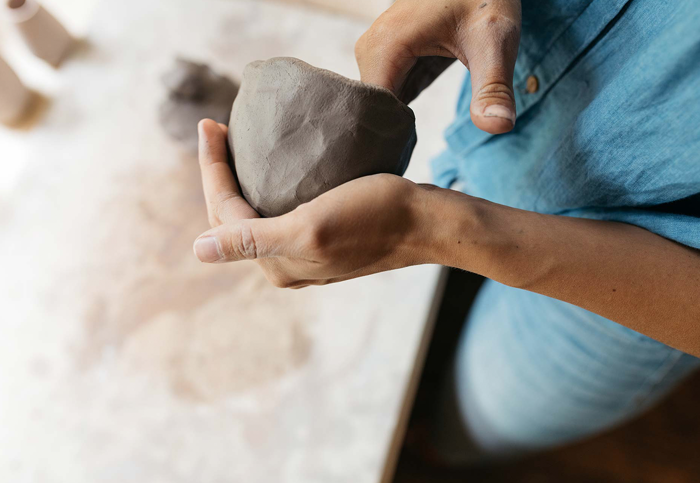 Close-up of hands cradling a rough clay ball in a ceramics studio