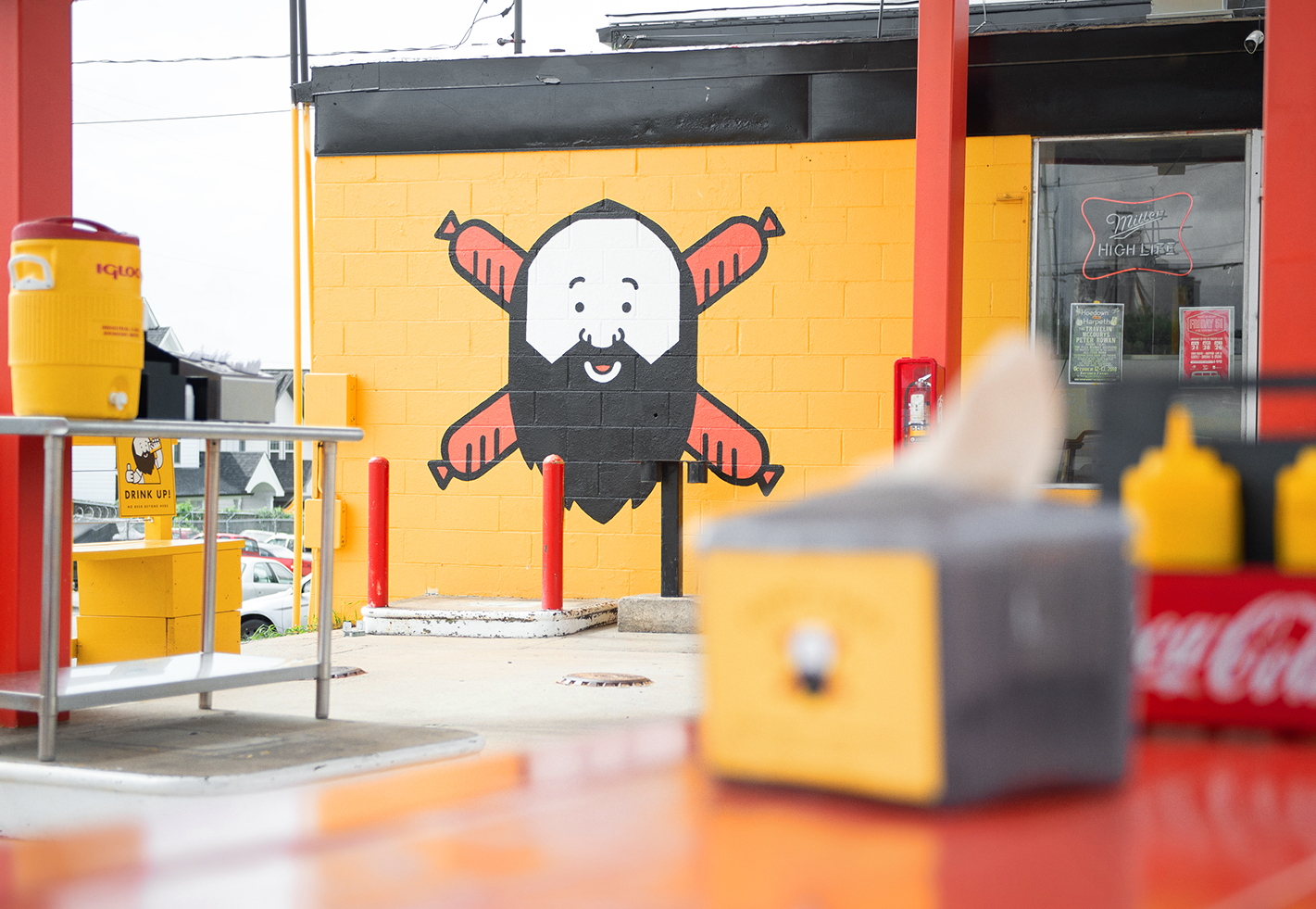 Daddy's Dogs yellow building exterior with the bearded mascot holding crossed hot dogs painted as a large mural