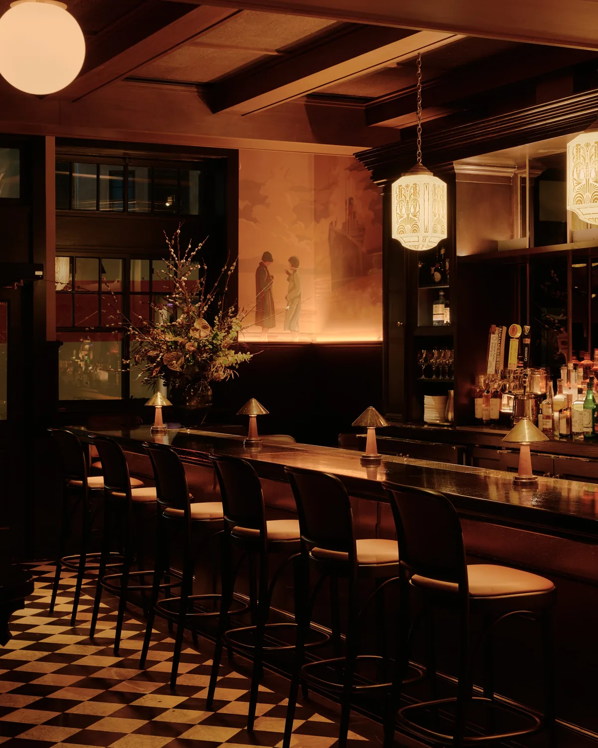Full bar interior at Izzy's — black and white checkered floors, dark wood bar, pendant lights, and mural on the wall