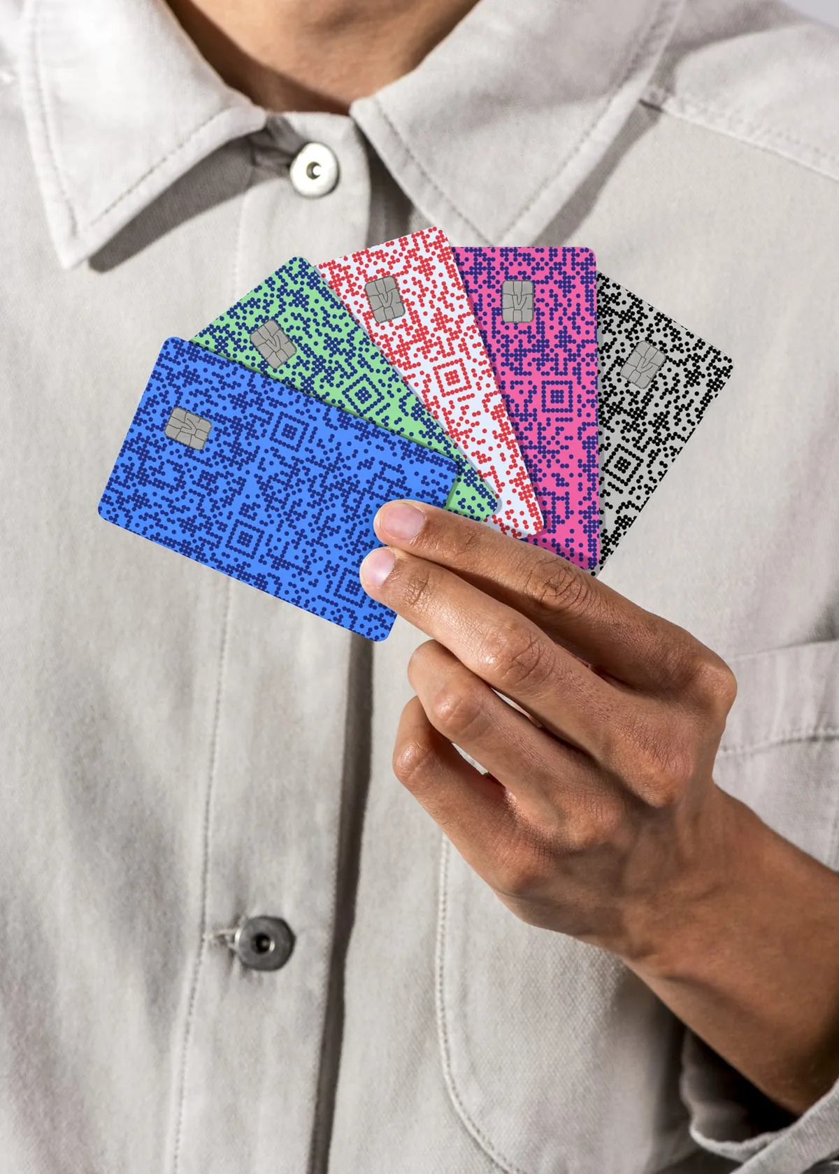 Hand holding five fanned-out Venmo credit cards in five different QR-code color designs — blue, green, red, pink, and black