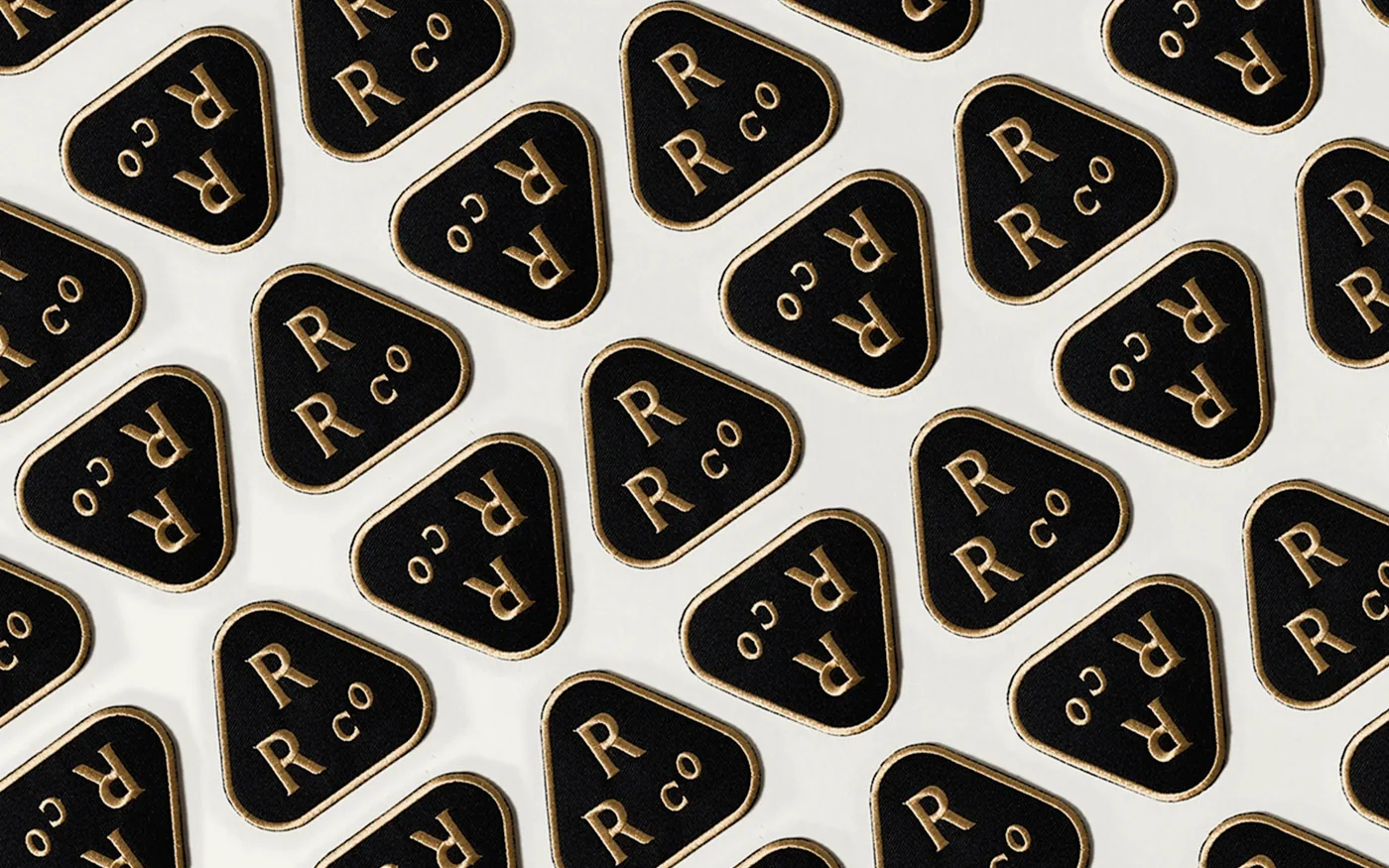 Repeat pattern of black and gold Rainier Roofing enamel patches on white background