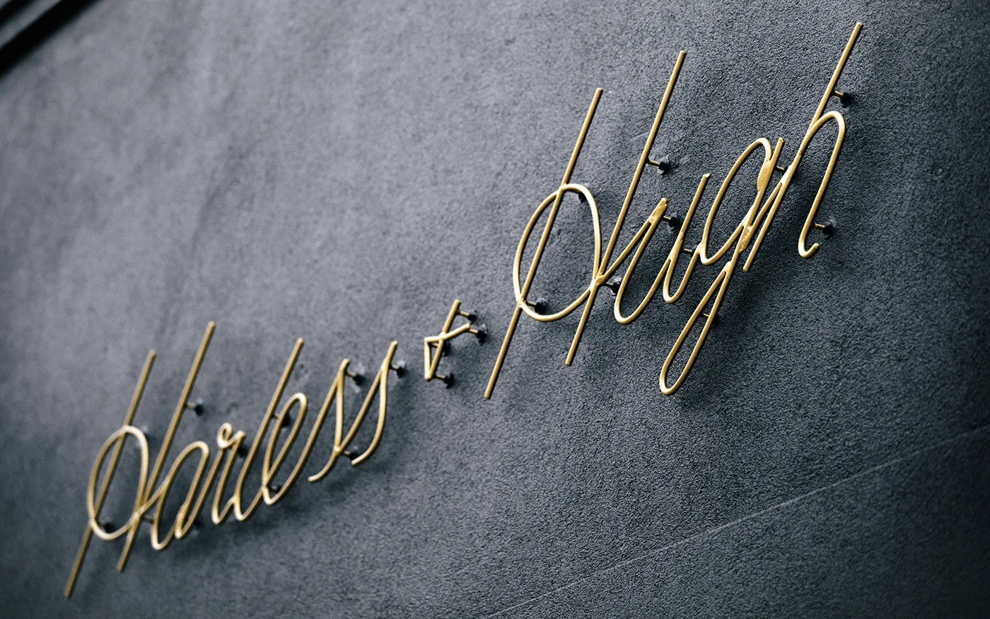 Gold script Harless and Hugh lettering mounted on a dark gray textured wall exterior