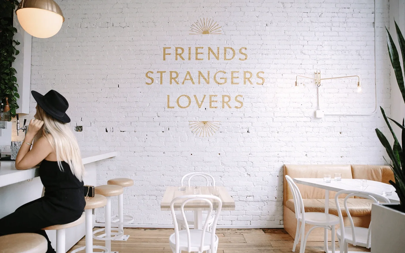 Bright white restaurant interior with Friends Strangers Lovers painted in gold script on a white brick wall