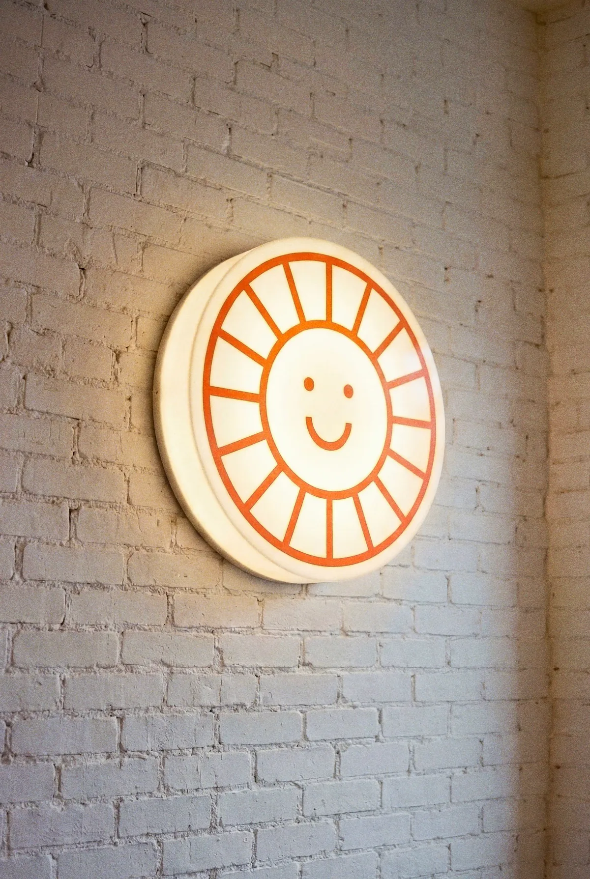 Illuminated Daypass sun logo sign mounted on a brick wall at night