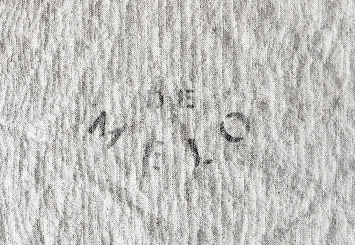 De Melo brand name stamped in gray ink on wrinkled linen fabric