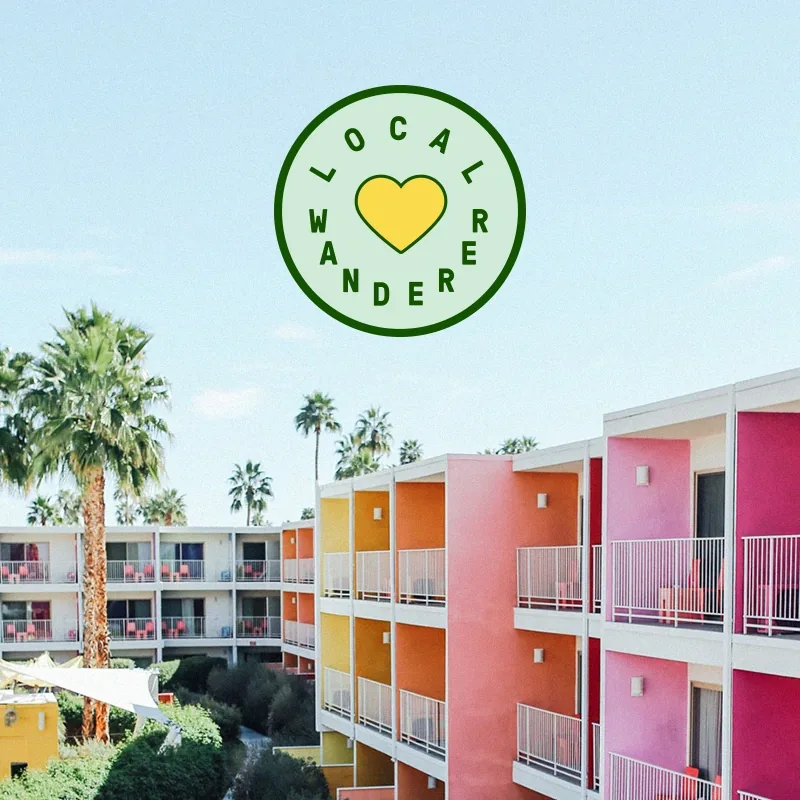 Colorful pink and orange motel exterior with Local Wanderer heart logo overlaid in green above it