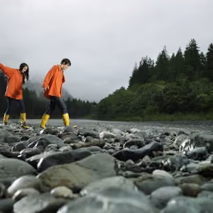 Couple walking across rocks of river bank.