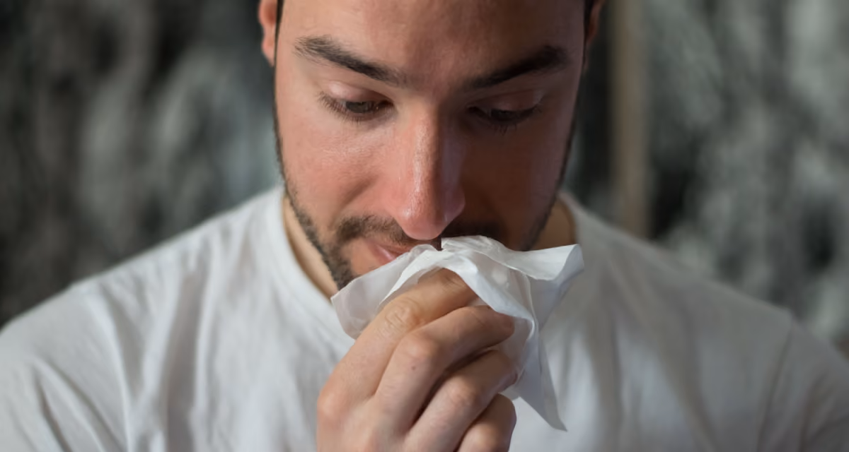Homme éternuant dans un mouchoir en extérieur au printemps, symptôme typique de l'allergie saisonnière au pollen