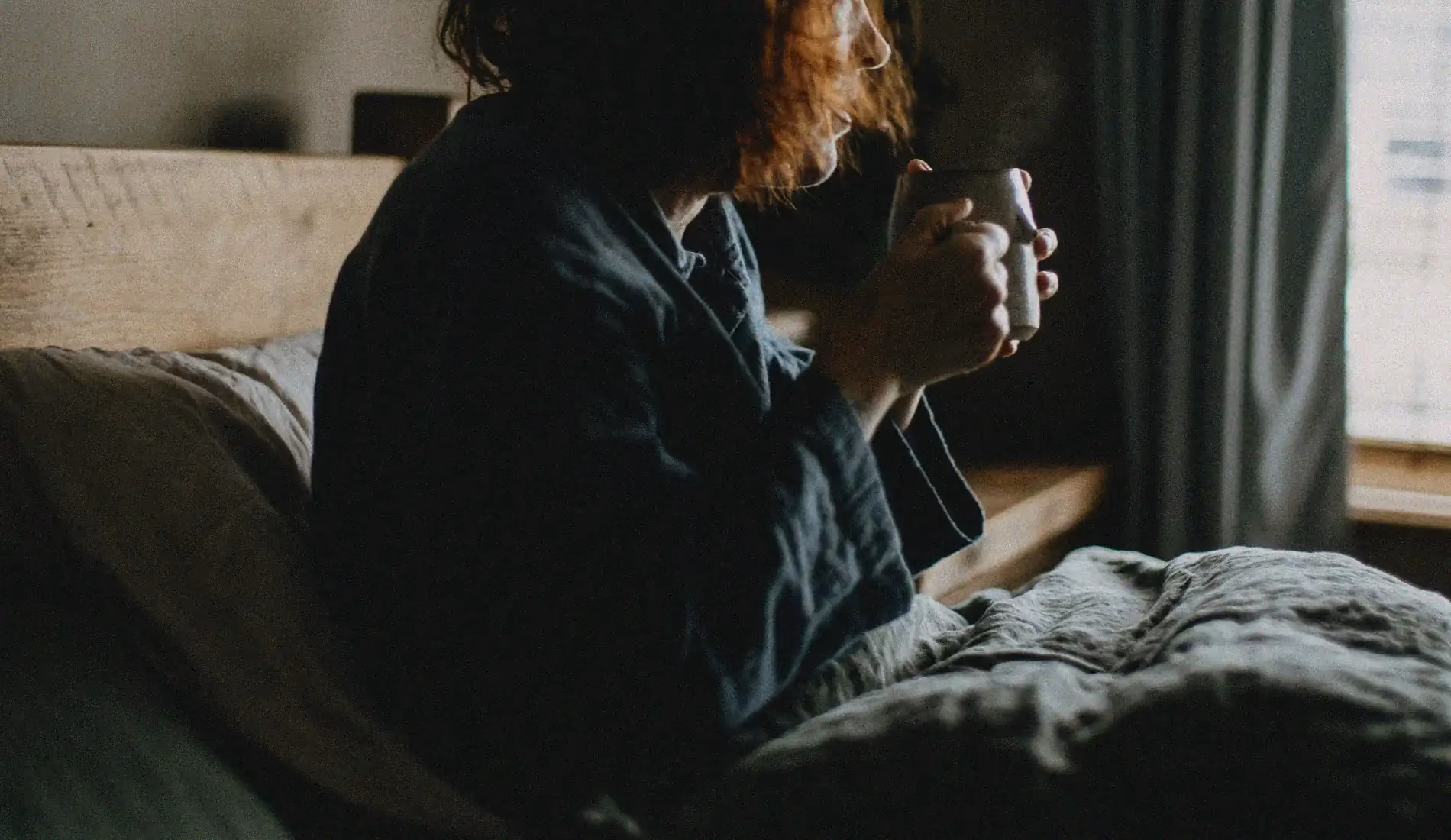Une femme assise dans son lit, en train de boire une tisane pour soulager ses douleurs pelviennes.
