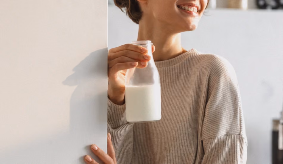 Une personne ouvre un frigo et en sort une bouteille de lait à moitié pleine