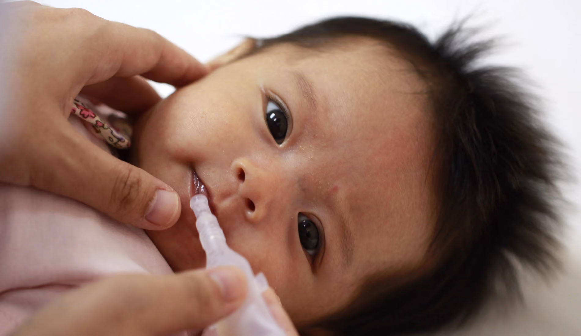 Un bébé couché, à qui un vaccin est en train d'être administré par la bouche