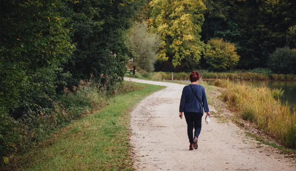 Une dame de dos, elle marche dans une allée bordée d'arbres.