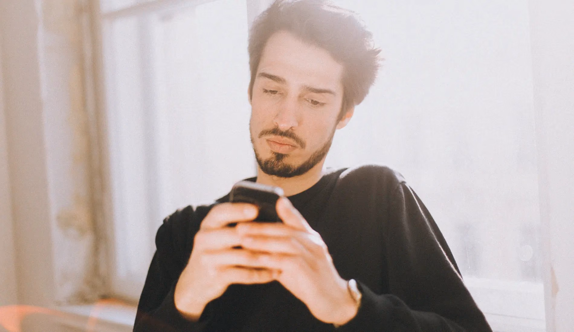 Un homme assis, en train de manipuler son téléphone. Il porte un polo noir.