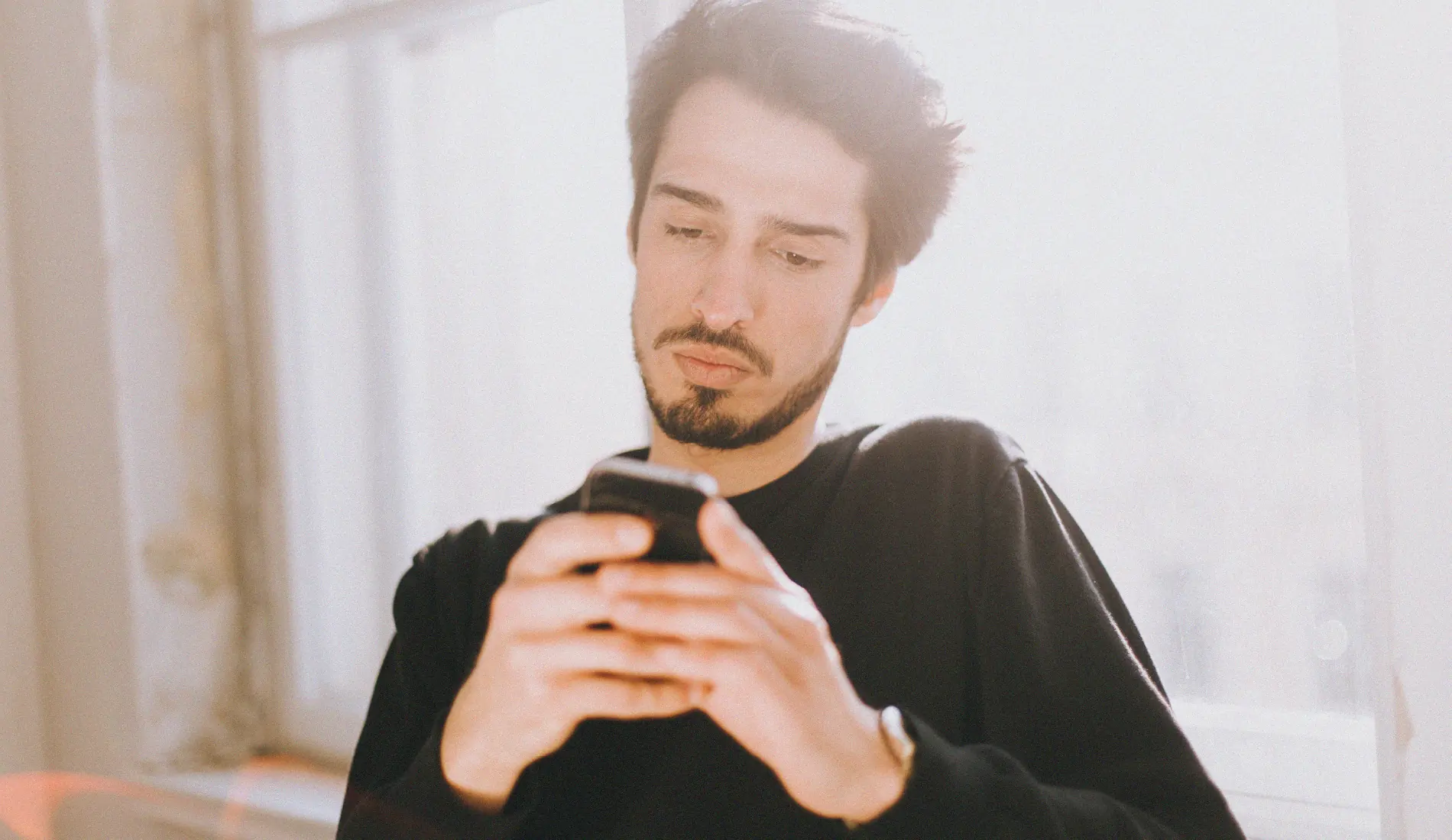 Un homme assis, en train de manipuler son téléphone. Il porte un polo noir.