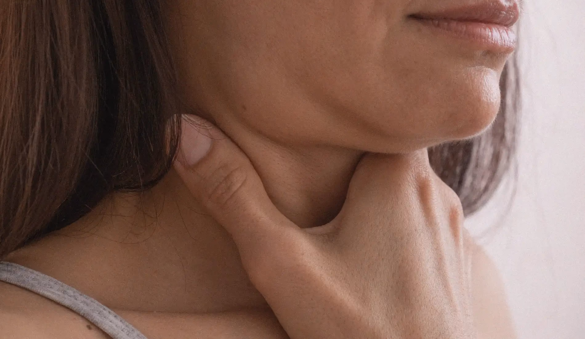 Une femme dont le visage est caché se tient la gorge avec sa main droite.