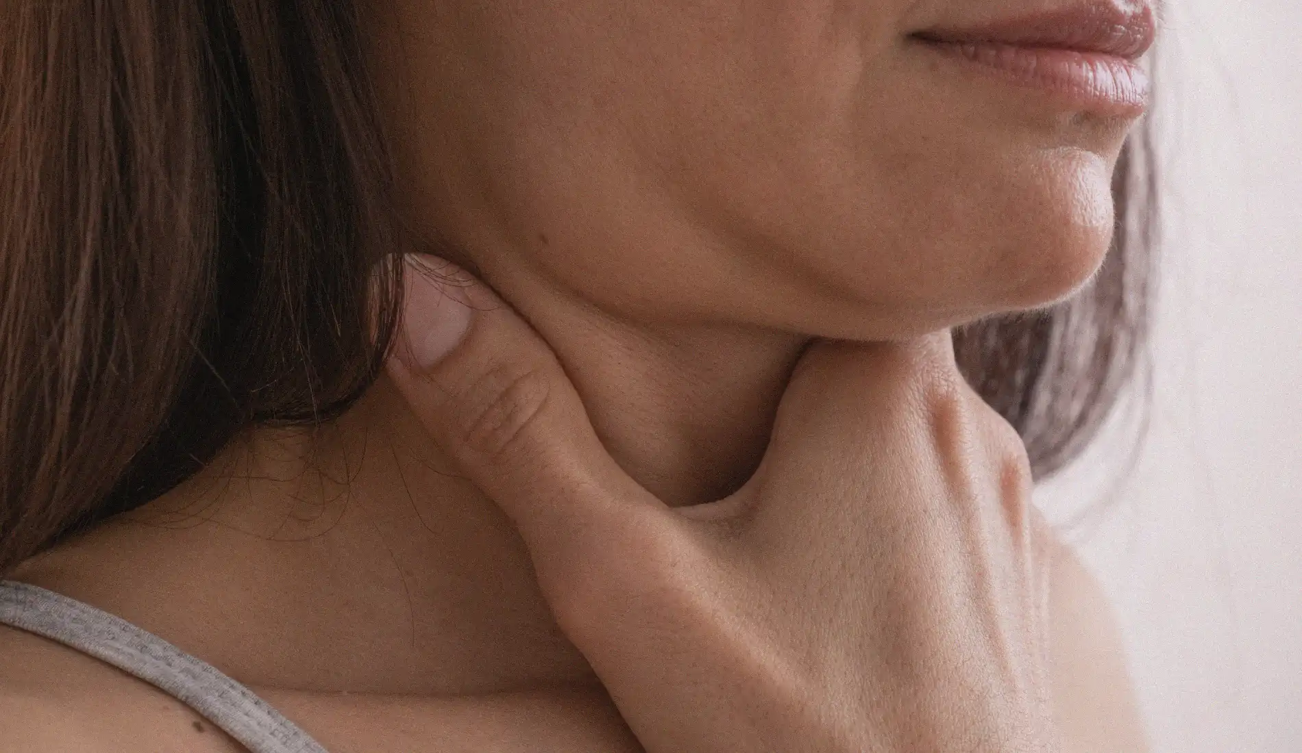Une femme dont le visage est caché se tient la gorge avec sa main droite.