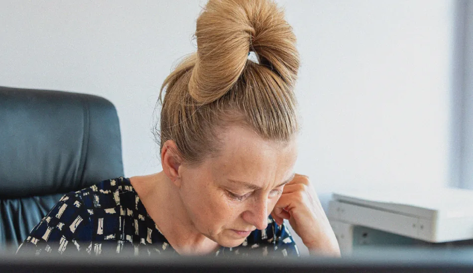 Une dame assise au bureau, la main posée sur la joue.