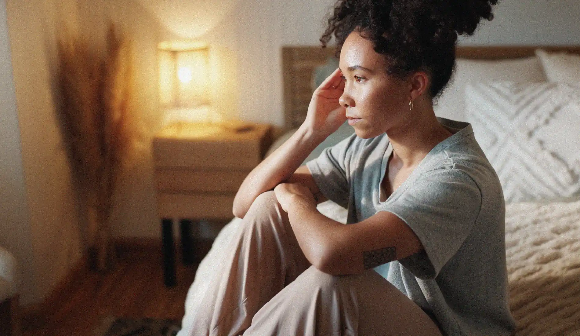 Une jeune femme assise, pensive, la main sur sa tempe droite.