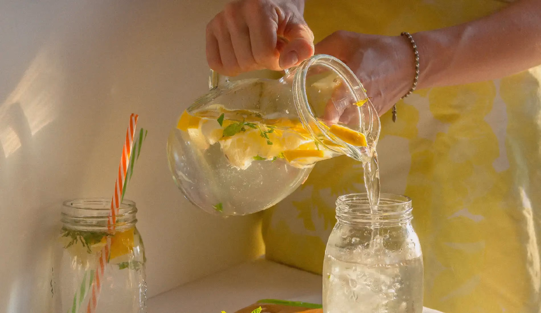 Une boisson détox composée de citron, contenue dans une carafe, en train d'être versée dans un verre.