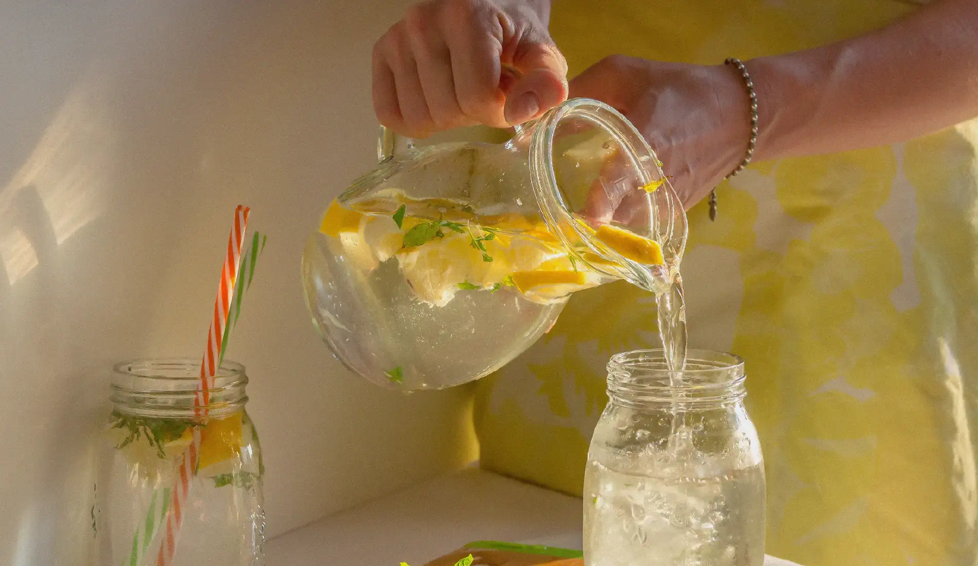 Une boisson détox composée de citron, contenue dans une carafe, en train d'être versée dans un verre.