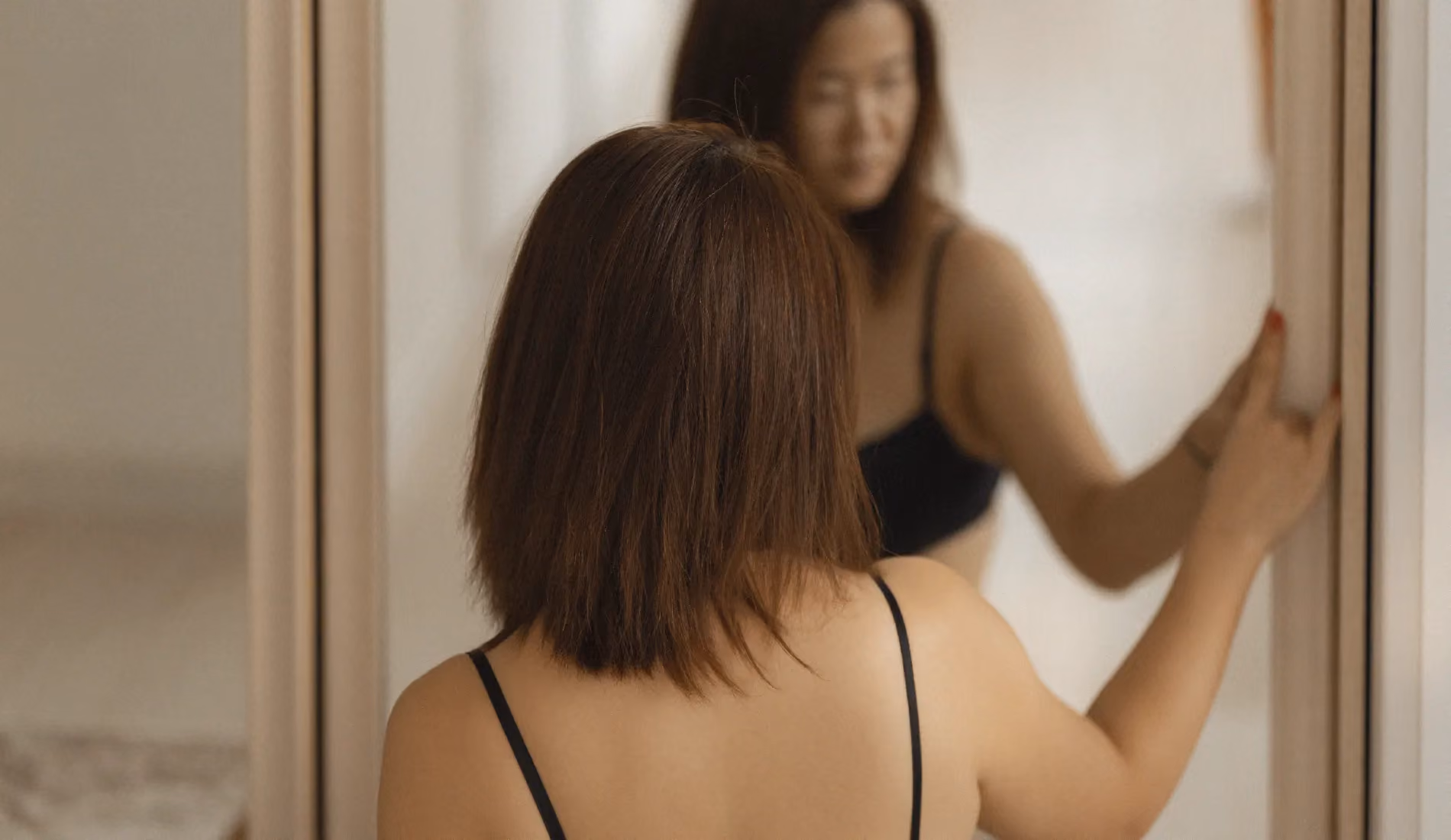 Une dame dont le visage a été flouté, se regarde dans un miroir. Elle a une forte corpulence.