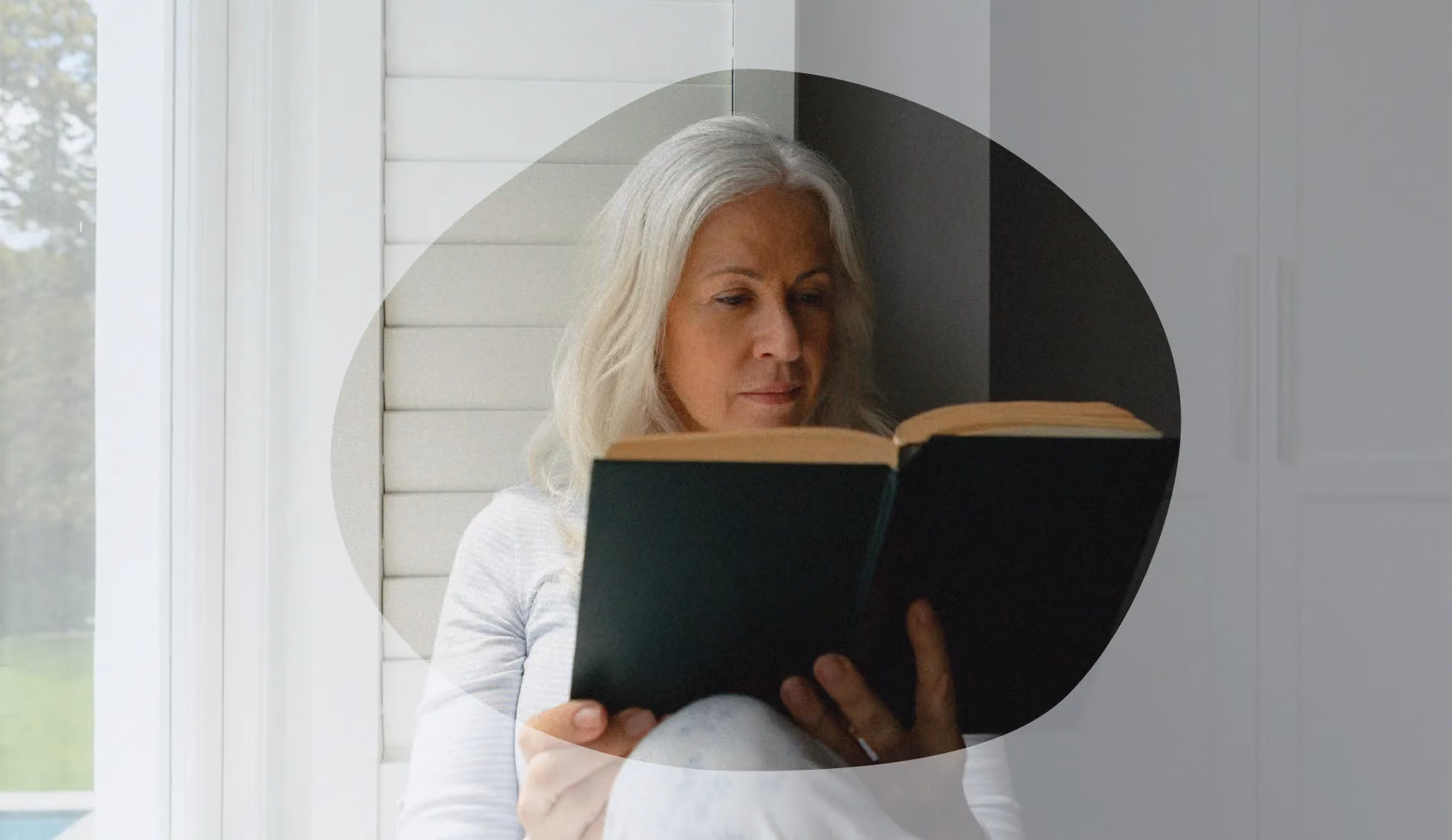 Préménopause. Une femme d'un certain âge, assise sur le rebord d'une fenêtre, en train de lire un livre.