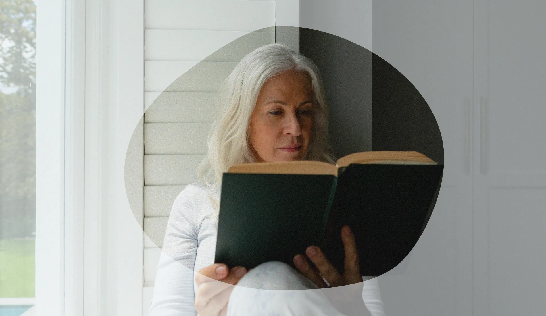 Préménopause. Une femme d'un certain âge, assise sur le rebord d'une fenêtre, en train de lire un livre.