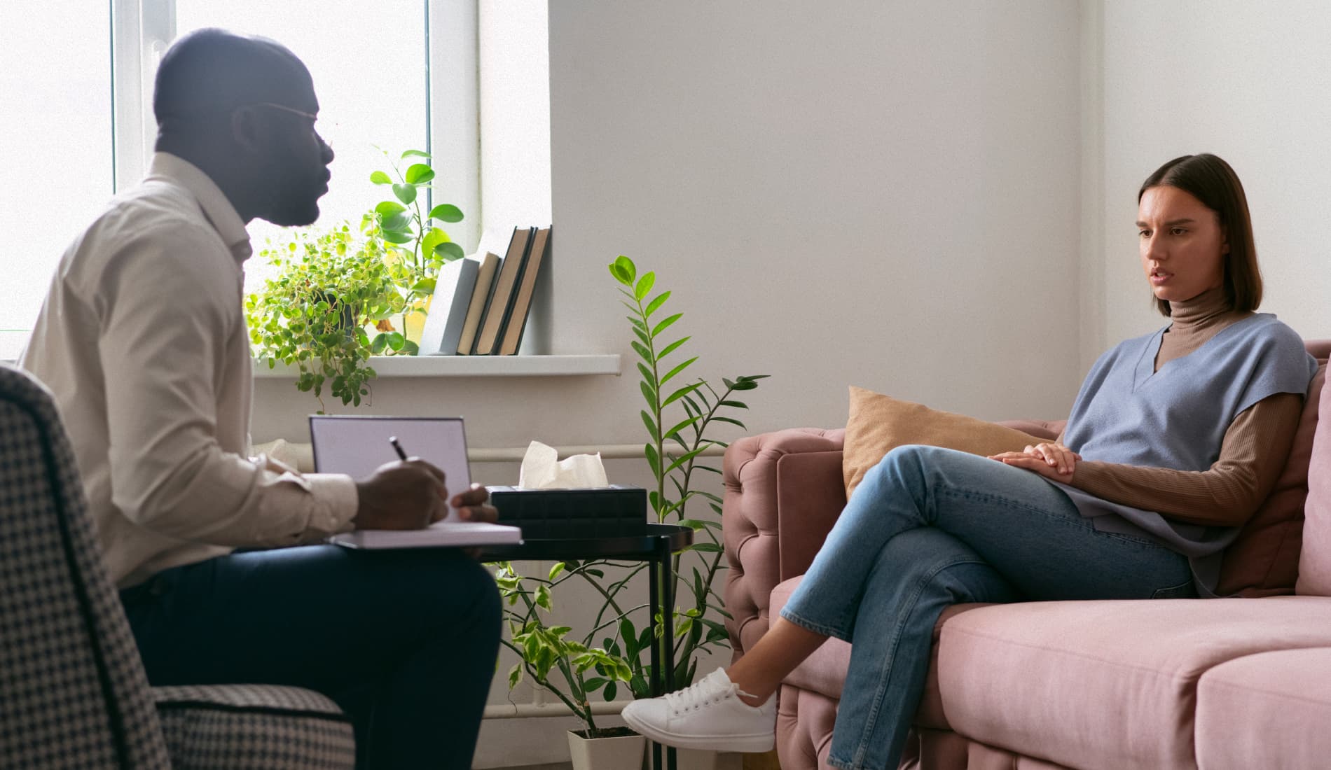 Séance avec un psychologue. Une femme assise sur un canapé. Un homme (psychologue) assis en face, un carnet dans la main.
