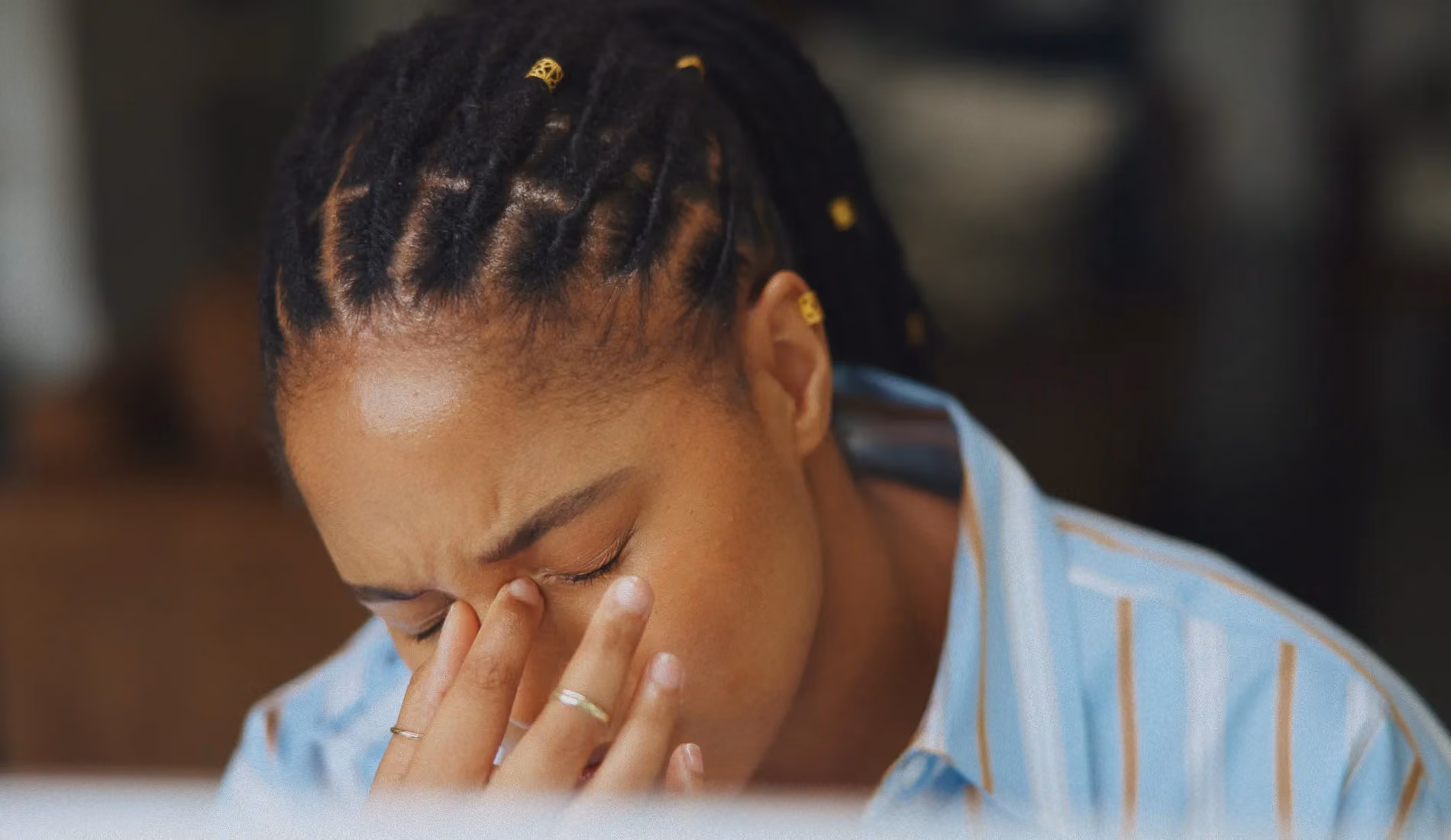 Jeune femme se pinçant l'arête du nez et fermant les yeux, geste de douleur typique d'une crise de migraine, en quête d'un moyen de la soulager rapidement.