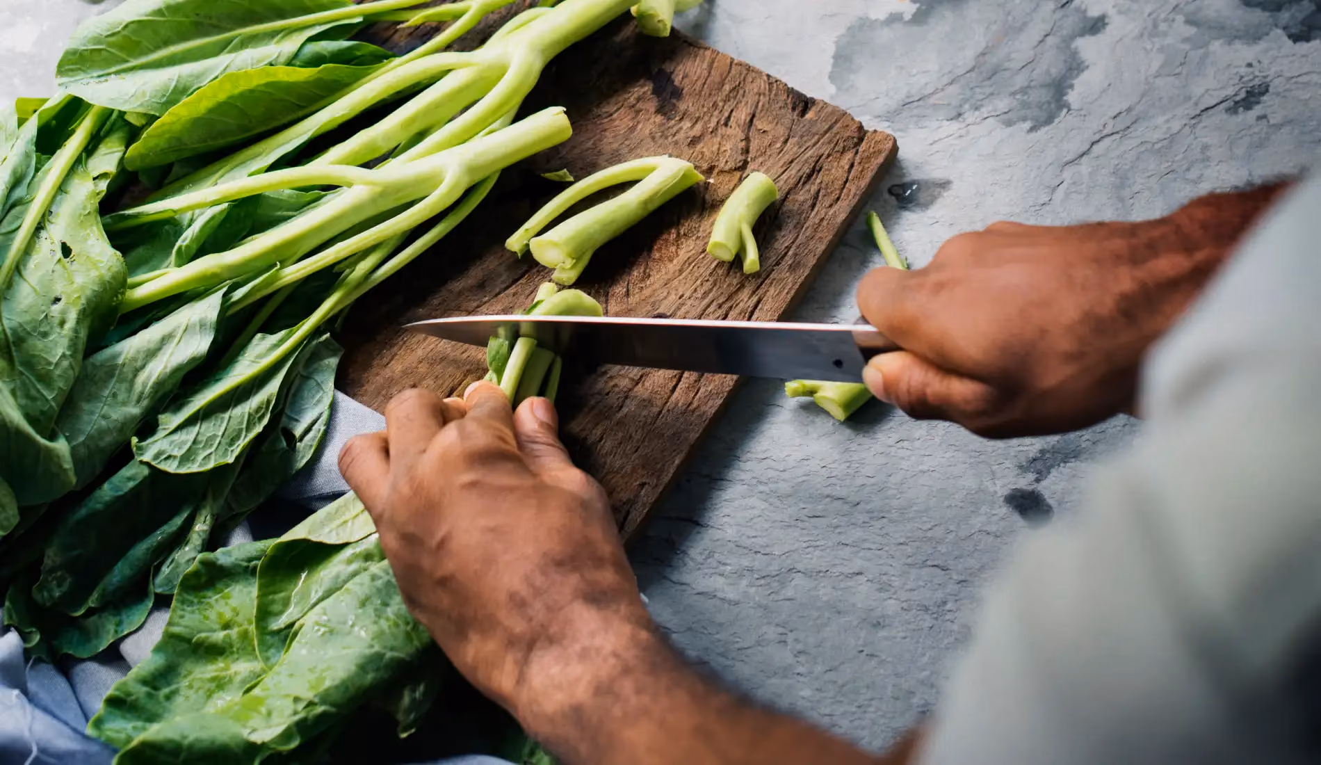Personne découpant des légumes verts, aliments riches en vitamine K dont la régularité de consommation est clé pour équilibrer un traitement par AVK (Coumadine, Sintrom, Previscan).
