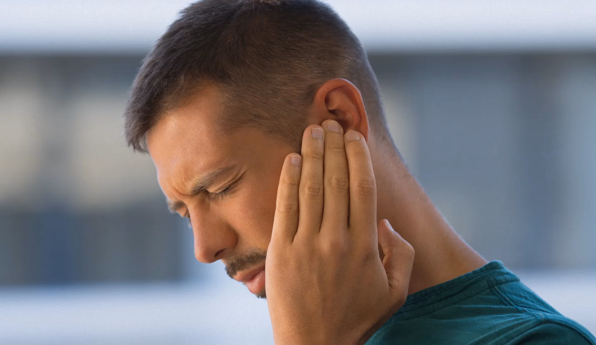 Une personne souffrant d'otite, qui se touche l'oreille en faisant la grimace.